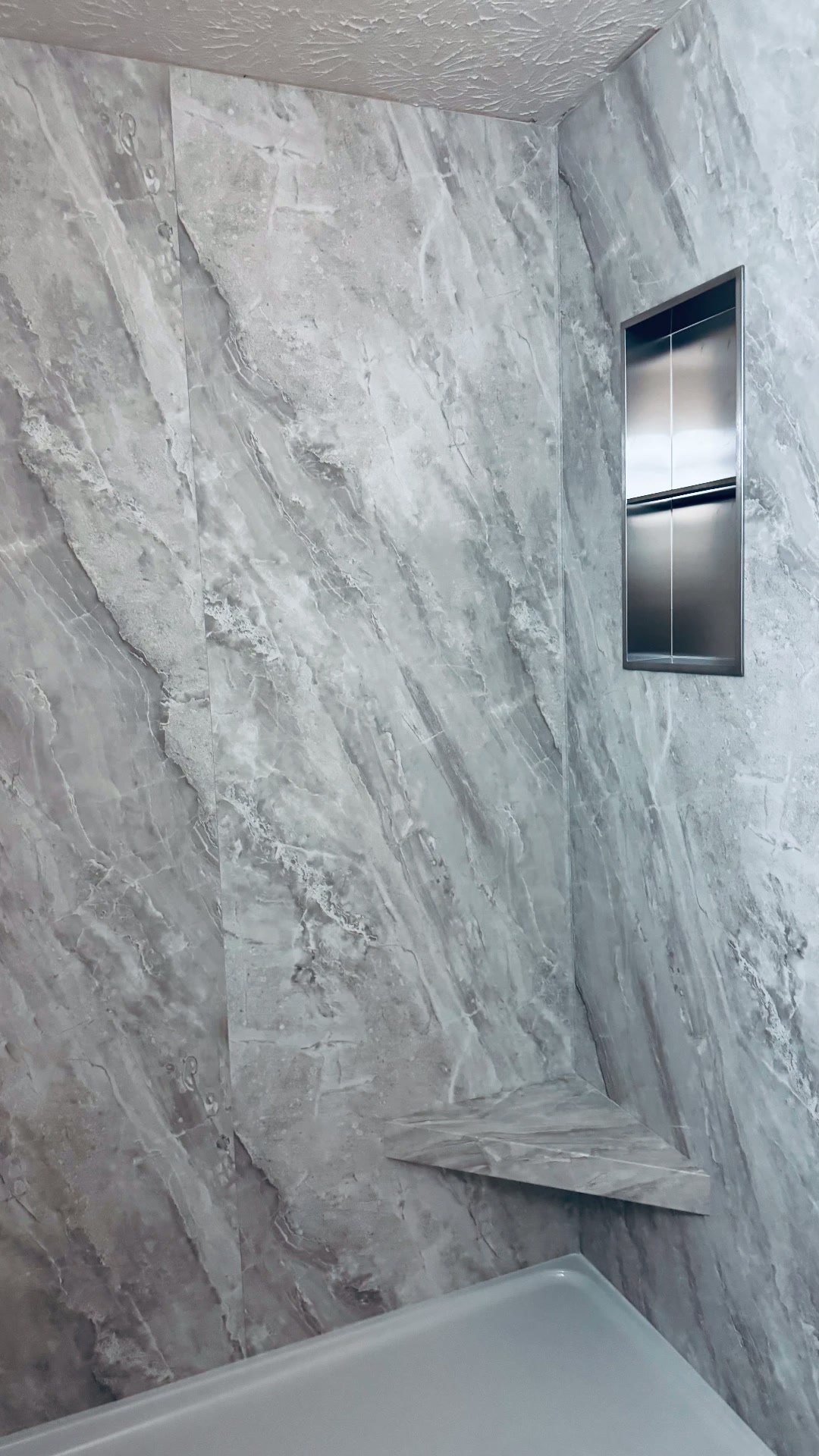 Gray stone shower surround with niche and corner shelf